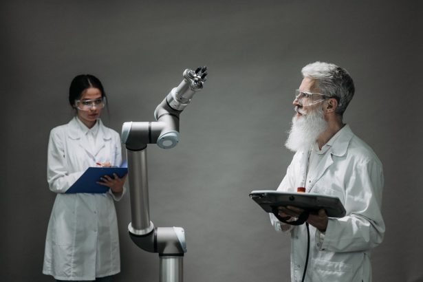 Dois pesquisadores de jaleco trabalham com um braço robótico em um laboratório.