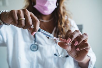 Profissional de saúde prepara uma seringa com vacina em ambiente clínico.