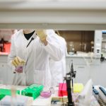 Cientista de jaleco e luvas manuseia amostras em um laboratório durante uma pesquisa.