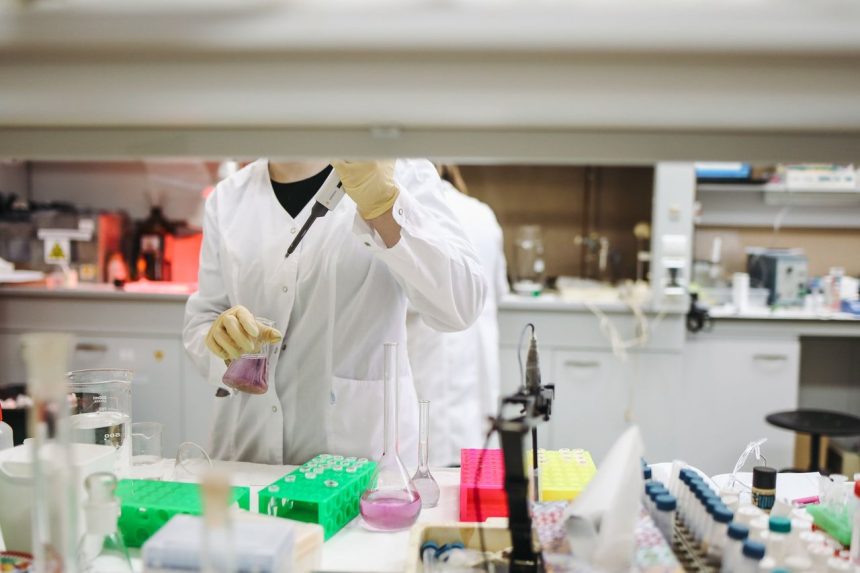 Cientista de jaleco e luvas manuseia amostras em um laboratório durante uma pesquisa.
